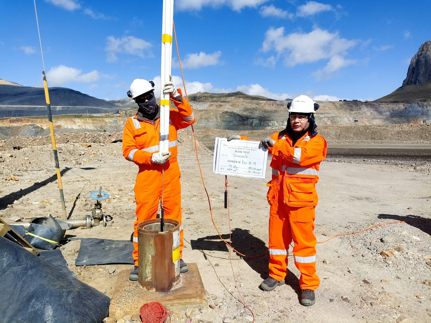 Two mine surveyors in orange coveralls and hard hats working at an open-pit site